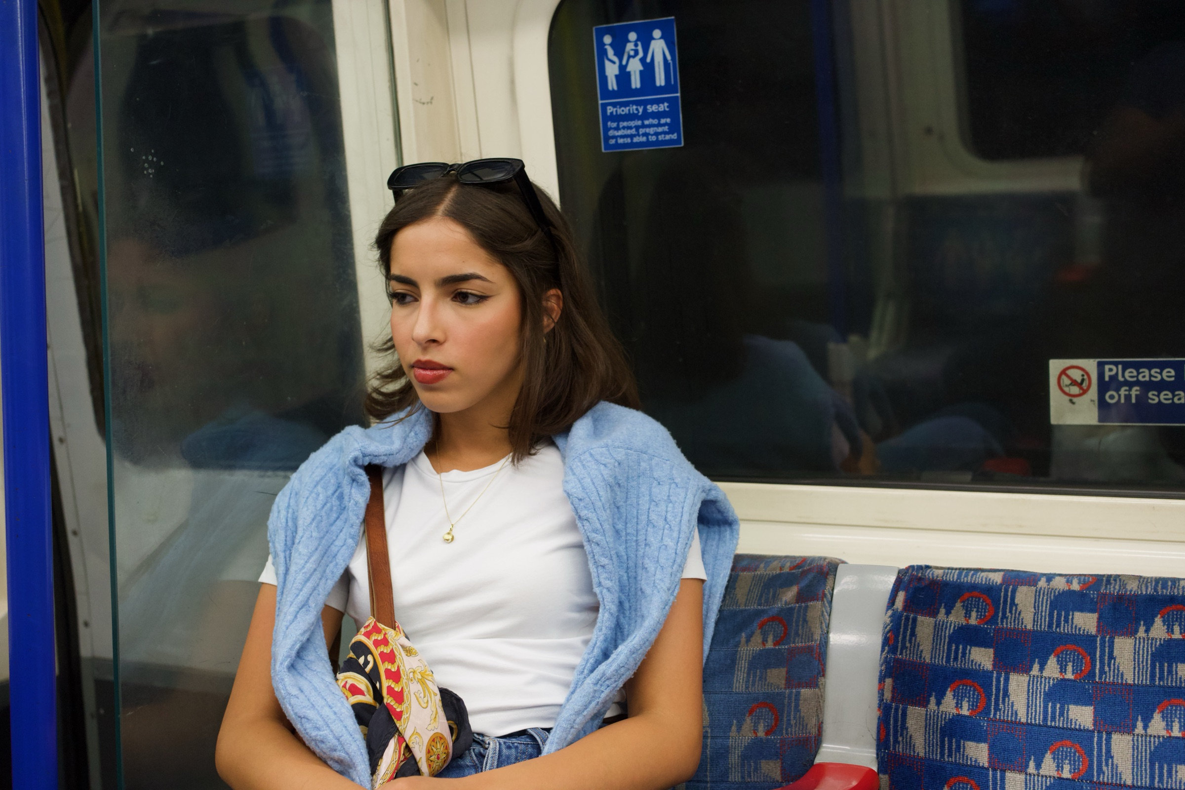 A woman lost in thought on the London Underground, the patterned seat fabric framing her stillness
