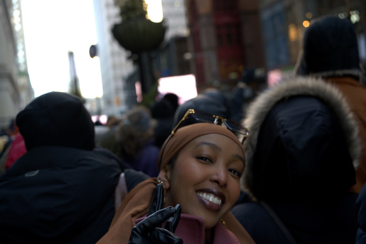 Woman in brown headscarf and leather gloves beams directly into the lens, crowd dissolving behind her on Inauguration Day